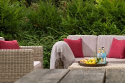 Outdoor patio with wicker furniture, red pillows, a blanket, and a tray with drinks, lemons, and snacks on a table.