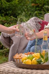 Two people toasting with gin and tonic drinks garnished with rosemary outdoors.