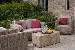 Outdoor wicker patio furniture set with red cushions and a tray of drinks and snacks on the table.