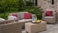 Outdoor wicker patio furniture set with red cushions and a tray of drinks and snacks on the table.