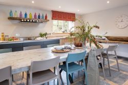 Modern kitchen with colorful bottles on shelf, a large dining table, and a floral centerpiece.