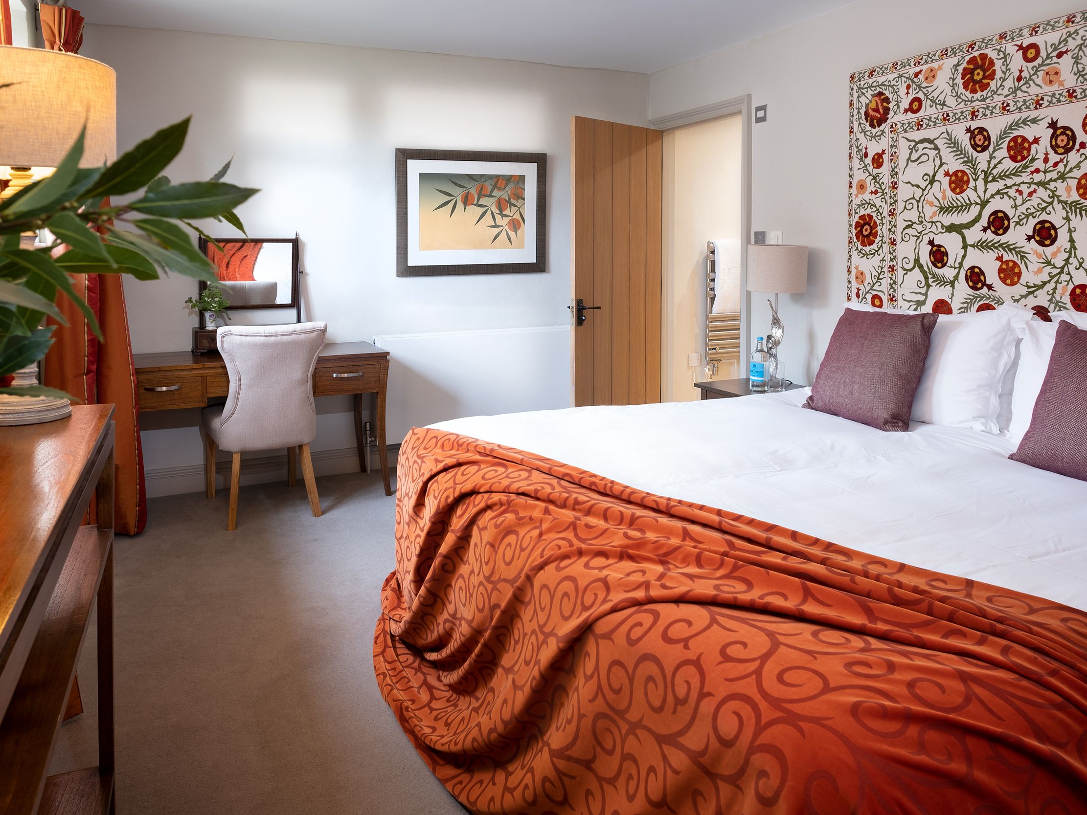 Cozy bedroom with orange accents, a double bed, desk, and decorative wall tapestry.