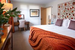 Cozy bedroom with orange accents, a double bed, desk, and decorative wall tapestry.