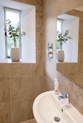 Modern bathroom with beige tiles, a white sink, a small mirror, and a window with a potted plant.
