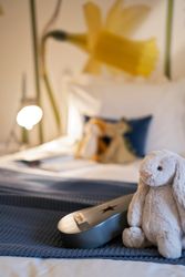 Plush rabbit toy and small guitar on a bed with blue blanket, daffodil wall art in the background