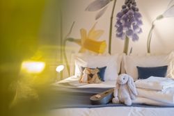 Cozy bed with stuffed animals, blue cushions, and a flower-themed wall mural