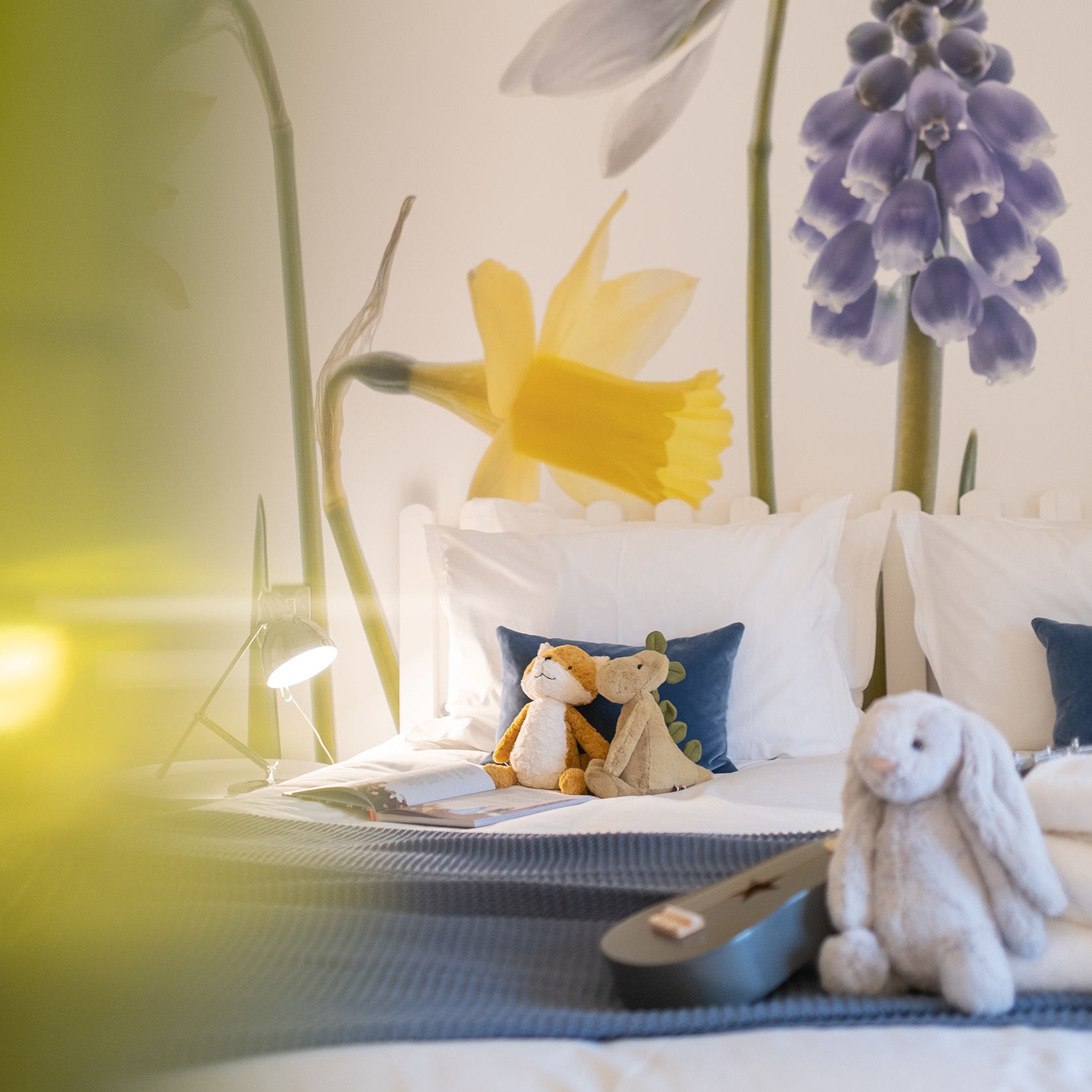 Cozy bed with stuffed animals and floral wall mural