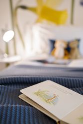 Children's book open on a blue knitted blanket with a cozy bedroom background.