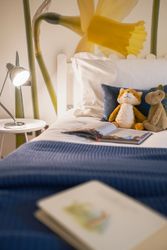 Cozy child's bed with stuffed animals, a book, and a daffodil mural