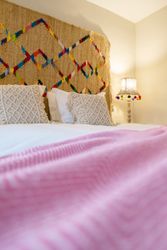 Cozy bed with textured pillows, a colorful wall hanging, and a lamp with a woven shade