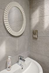 Modern bathroom sink area with round mirror, soap dispenser, and textured tile wall