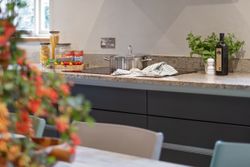 Modern kitchen countertop with a pot on the stove, jars of pasta, canned tomatoes, herbs, olive oil, and fresh vegetables.