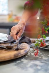 A hand placing forks on a wooden serving board next to a stack of plates.