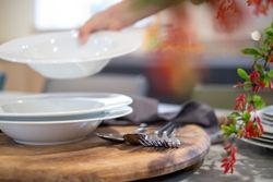 Hand setting white bowls on a table with cutlery on a wooden board