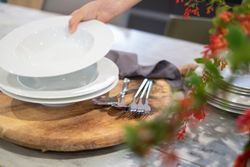 Hand setting white plates on a wooden board with cutlery nearby