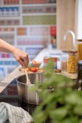 A person stirring a pot on a stovetop in a kitchen.