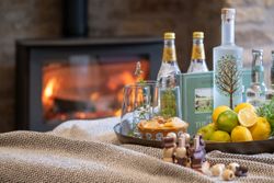 A cozy scene with drinks, lemons, snacks, and a blanket near a fireplace.
