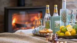 A cozy scene with drinks, lemons, snacks, and a blanket near a fireplace.