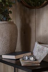 Eyeglasses resting on a folded map beside a book and a large vase with green foliage.
