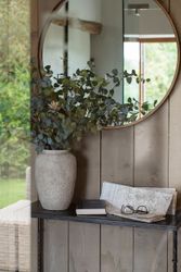 Vase with green eucalyptus branches on a table, a round wall mirror, book, map, and eyeglasses