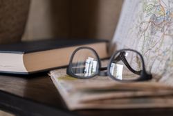 A close-up of a pair of eyeglasses resting on a folded map with a closed book in the background.