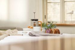 Breakfast tray on bed with coffee, bread, pastries, and flowers.