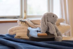 Stuffed gray bunny sitting on a black guitar with folded towels in the background