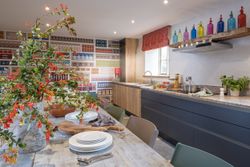 Modern kitchen with colorful decor, open shelving, and a large floral centerpiece on the dining table.