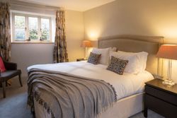 Cozy bedroom with large bed, patterned pillows, bedside lamps, and window with floral curtains