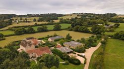 Aerial view of a large countryside estate with multiple stone buildings, driveways, and surrounding green fields and trees.
