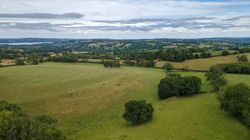 Aerial view of green fields and rolling hills under a partly cloudy sky