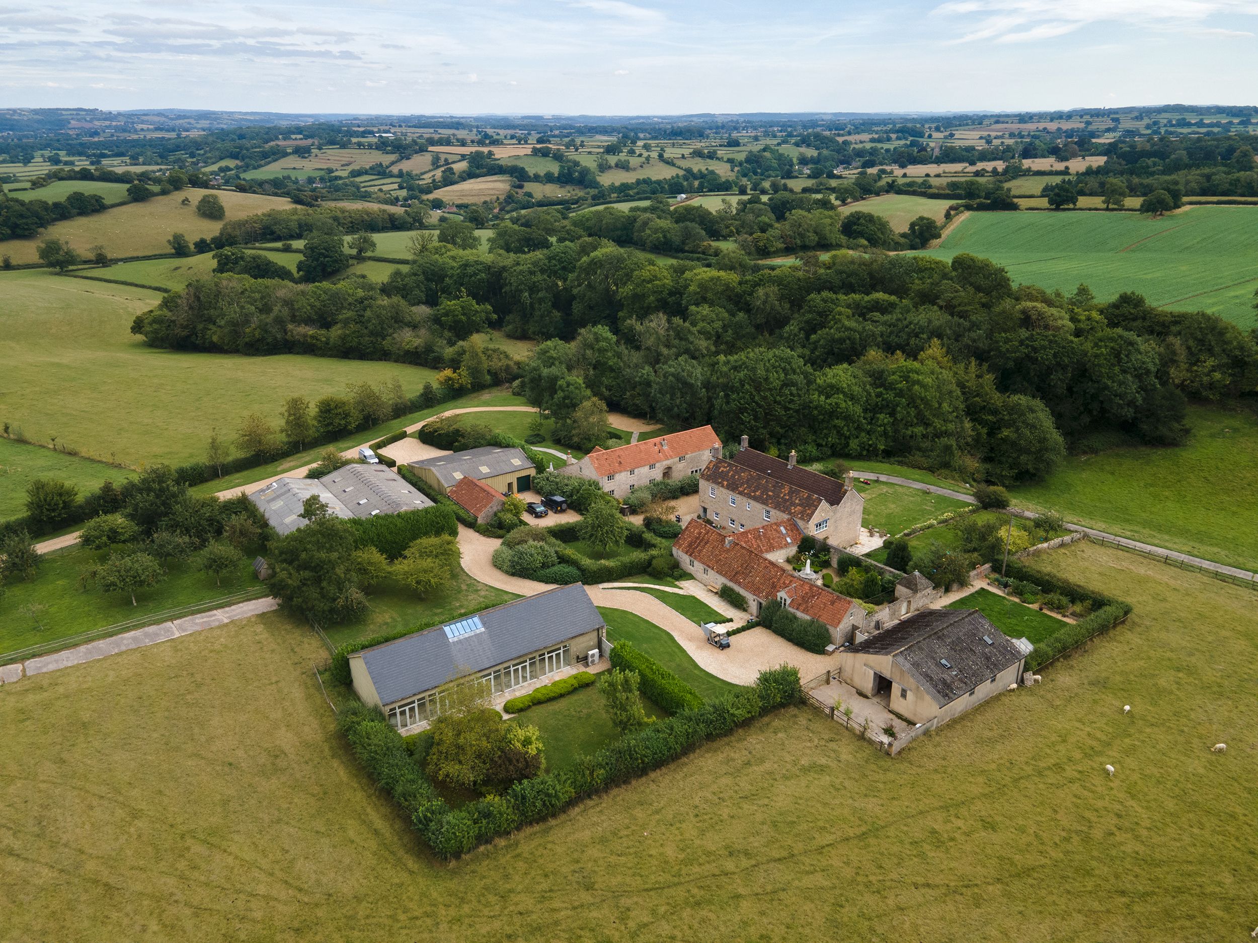 Aerial view of a large rural property with several farm buildings and houses surrounded by green fields and trees.