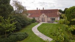 Traditional stone house with red tiled roof and a landscaped garden featuring a stone pathway.