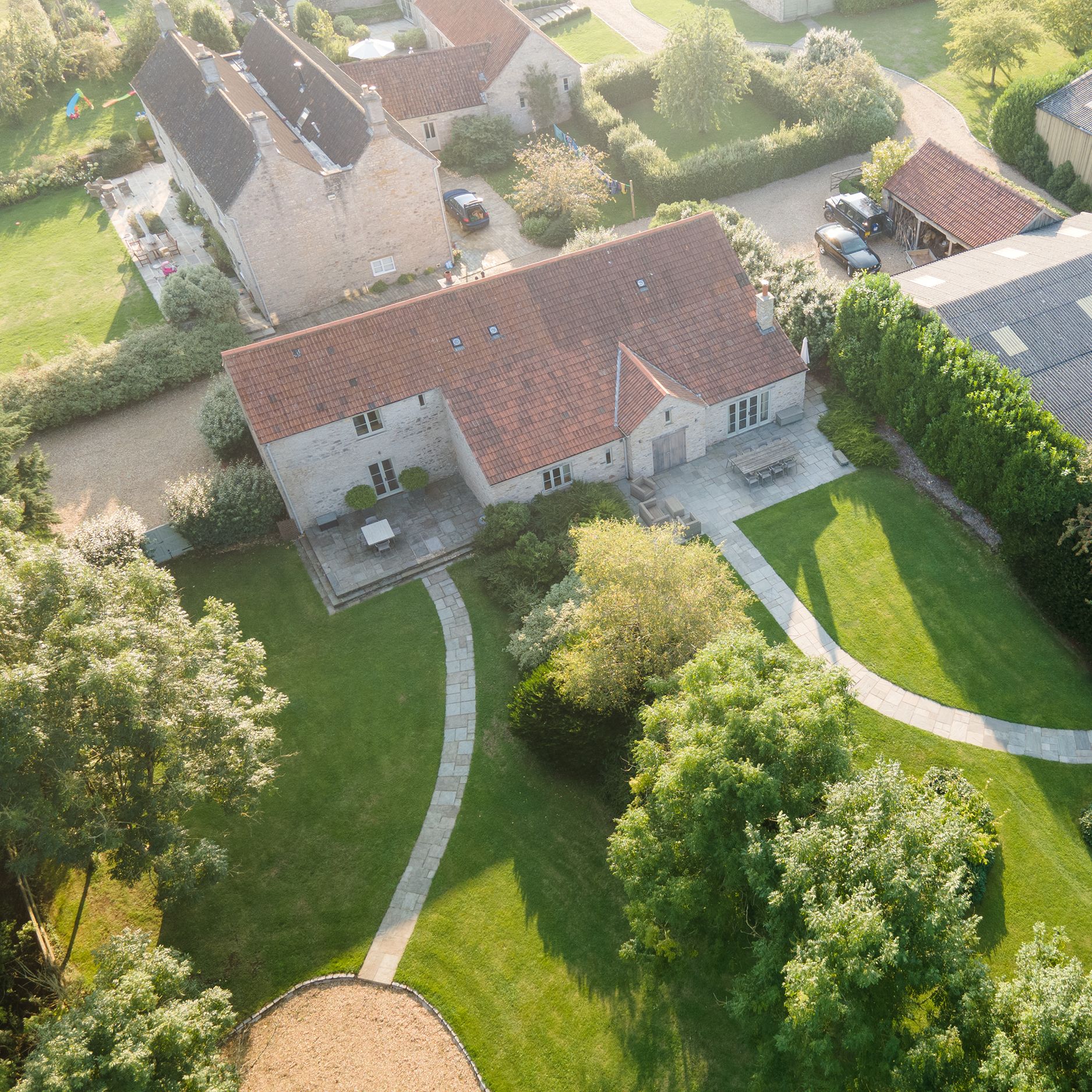Aerial view of a countryside property with a stone house, red-tiled roof, garden paths, and surrounding greenery.