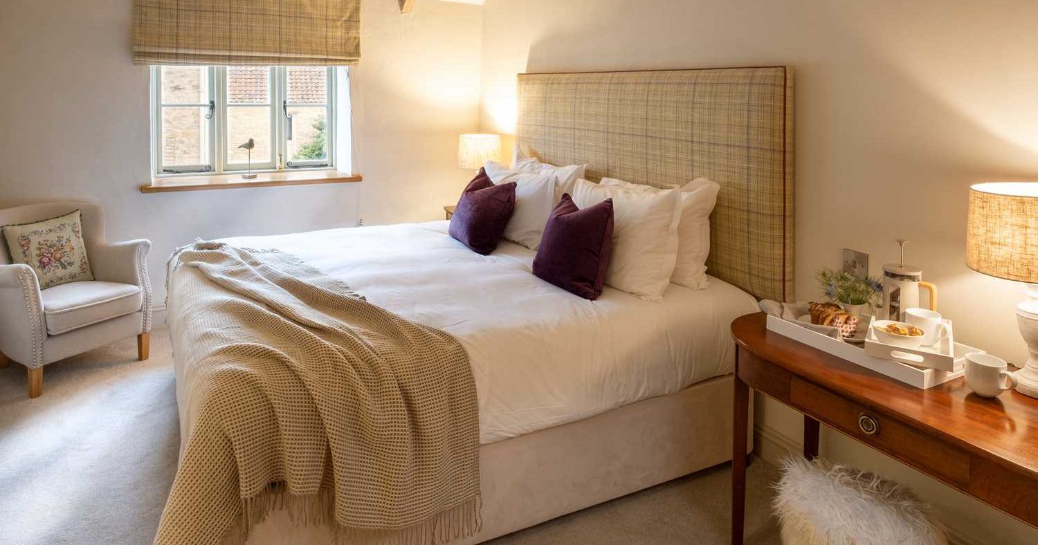 Cozy bedroom with large bed, neutral decor, and a tray with breakfast on a wooden table