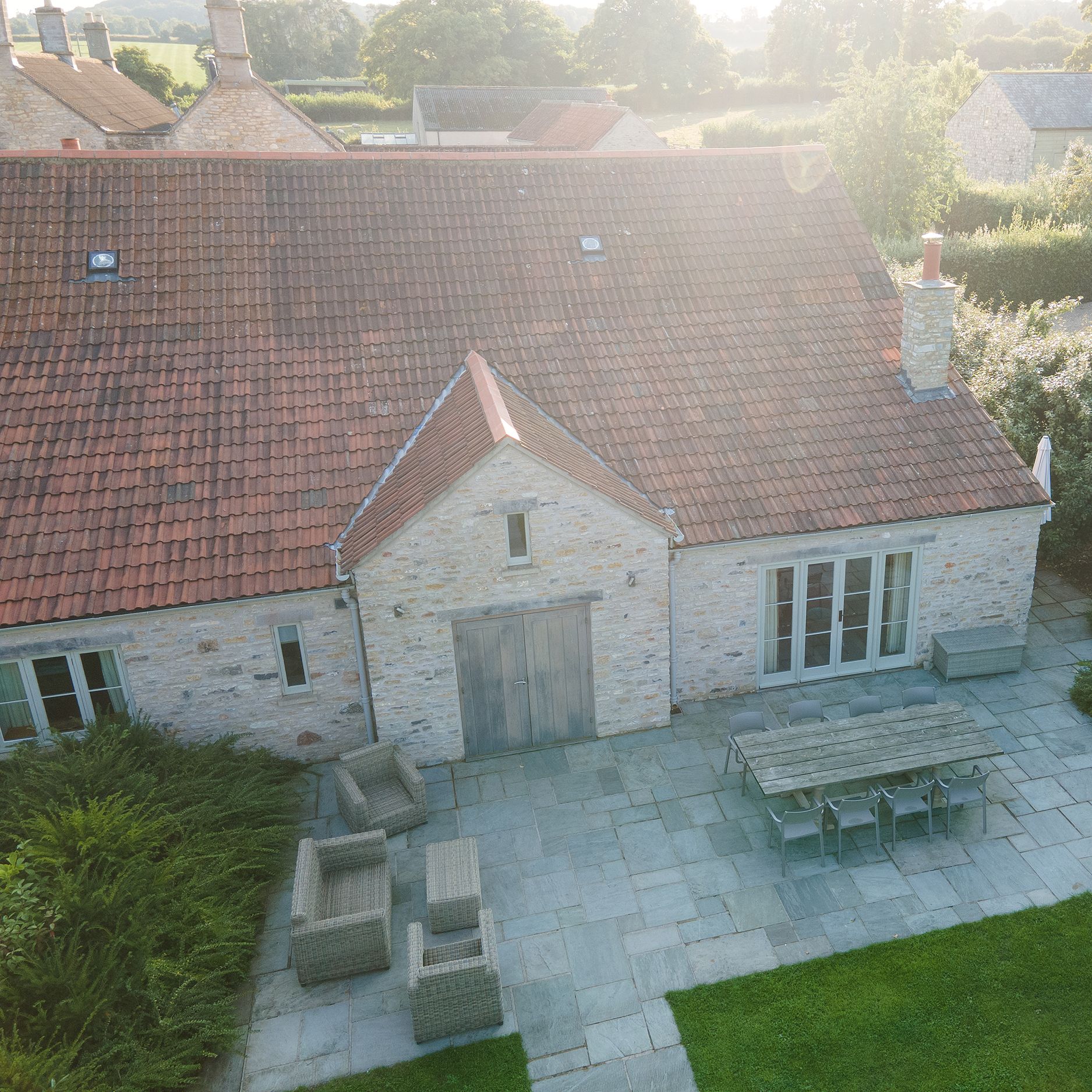 Aerial view of a stone house with a red-tiled roof and a large patio with outdoor seating.