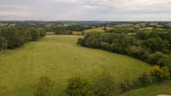 Aerial view of a rural landscape with green fields and scattered trees under a cloudy sky.