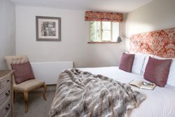 Cozy bedroom with a double bed, decorative headboard, pillows, fur throw, and an open book with glasses.