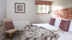 Cozy bedroom with a double bed, decorative headboard, pillows, fur throw, and an open book with glasses.