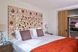 Cozy bedroom with a colorful embroidered tapestry behind the bed and an open closet.