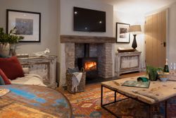 Cozy living room with stone fireplace, wood-burning stove, rustic furniture, and colorful rug