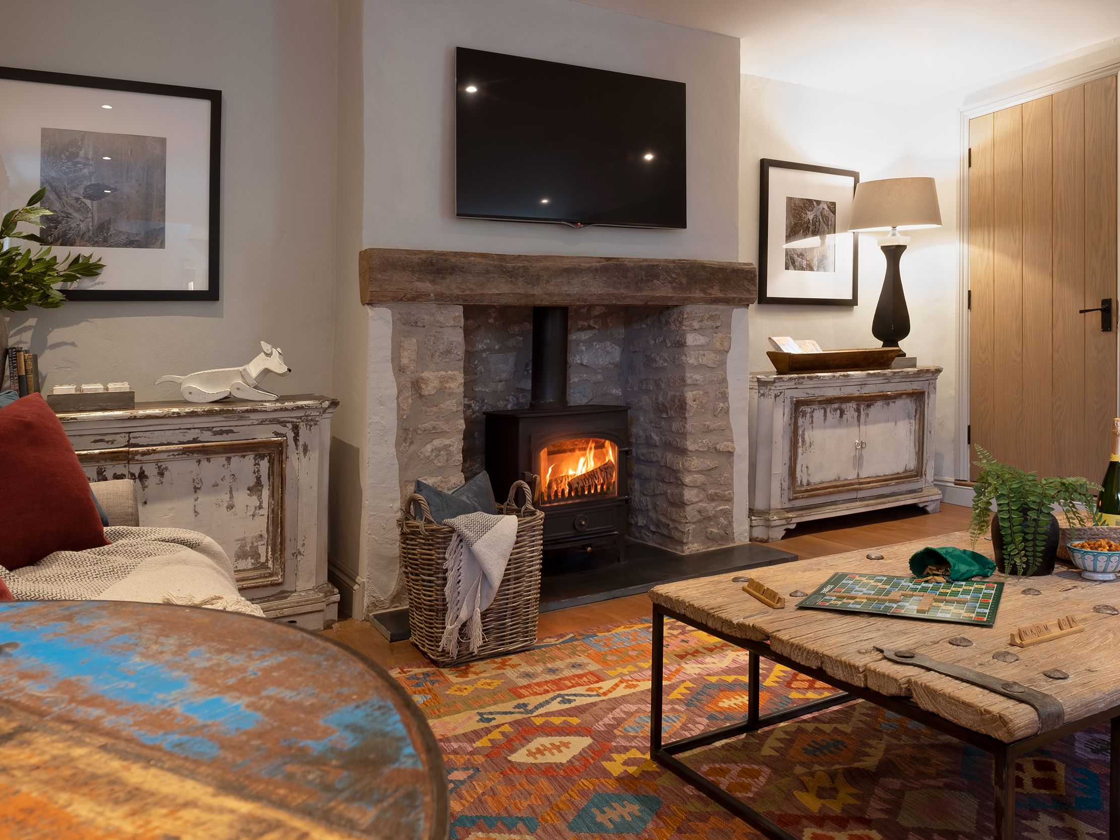 Cozy living room with stone fireplace, wood-burning stove, rustic furniture, and colorful rug