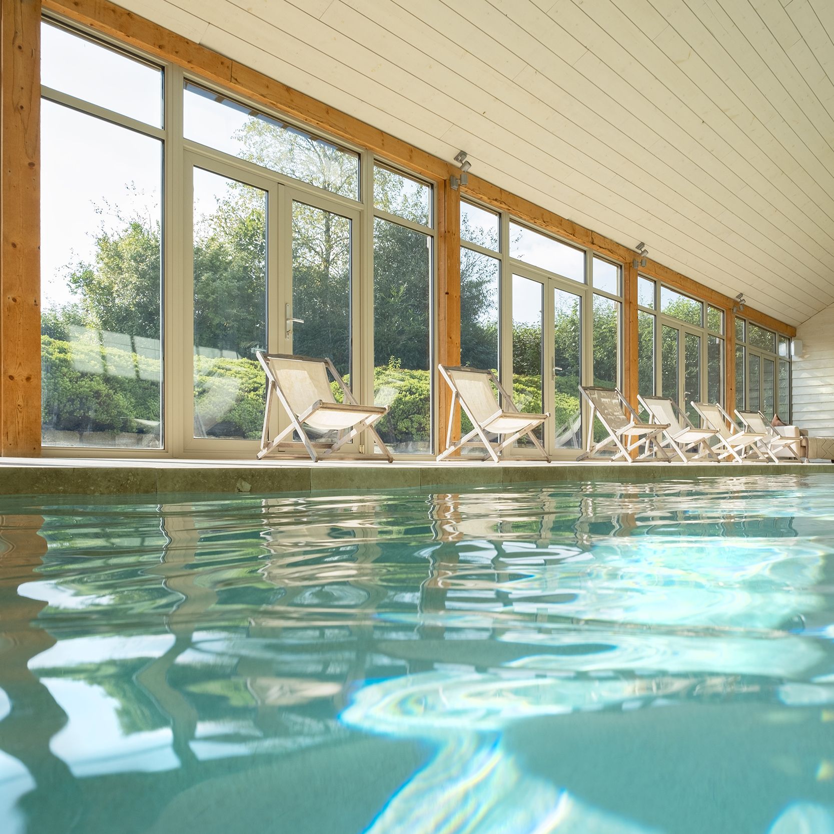 Indoor swimming pool with lounge chairs by large windows
