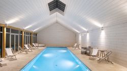 Indoor swimming pool with lounge chairs in a modern, white-paneled room