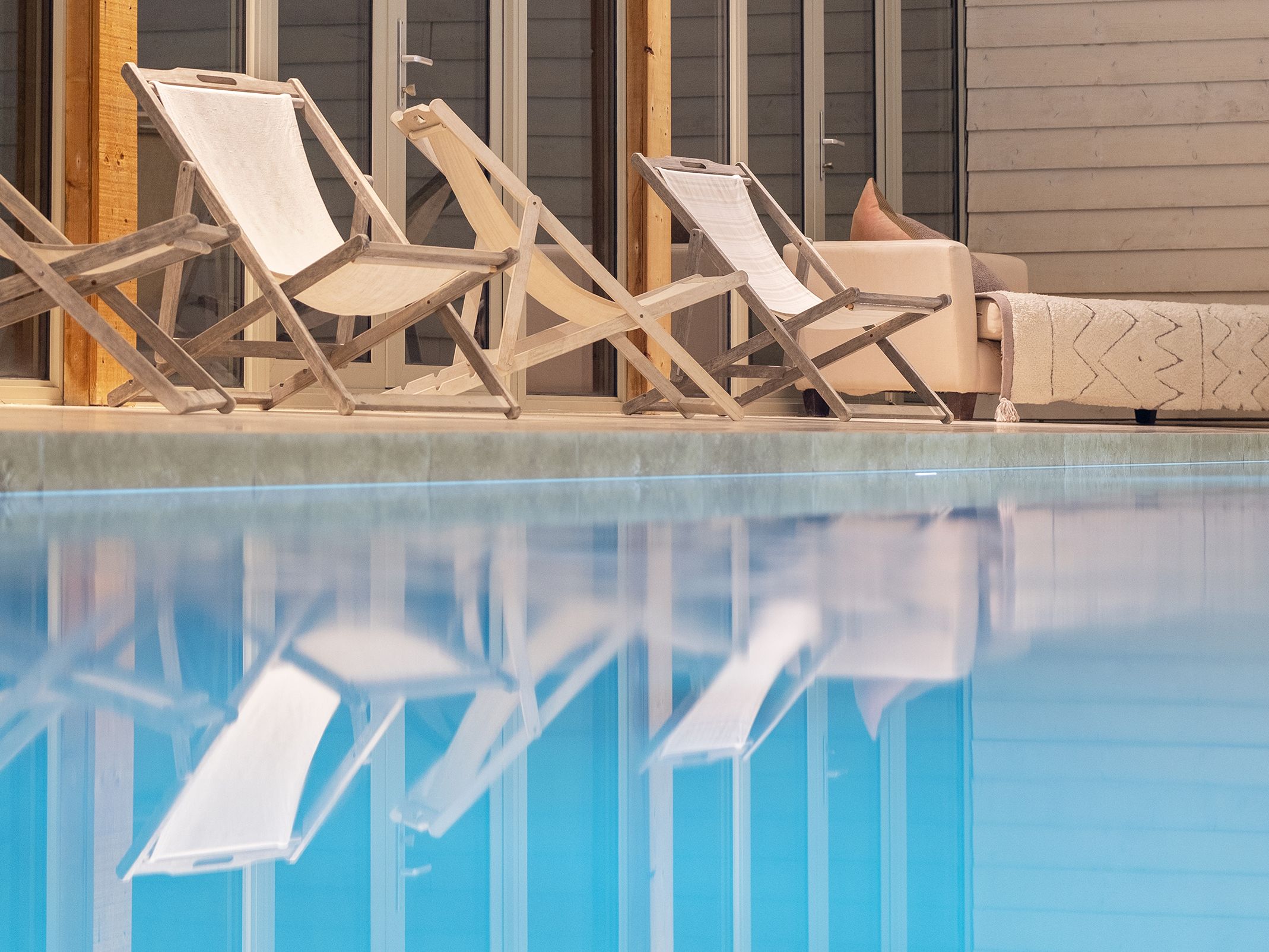 Wooden lounge chairs and a sofa next to an indoor swimming pool