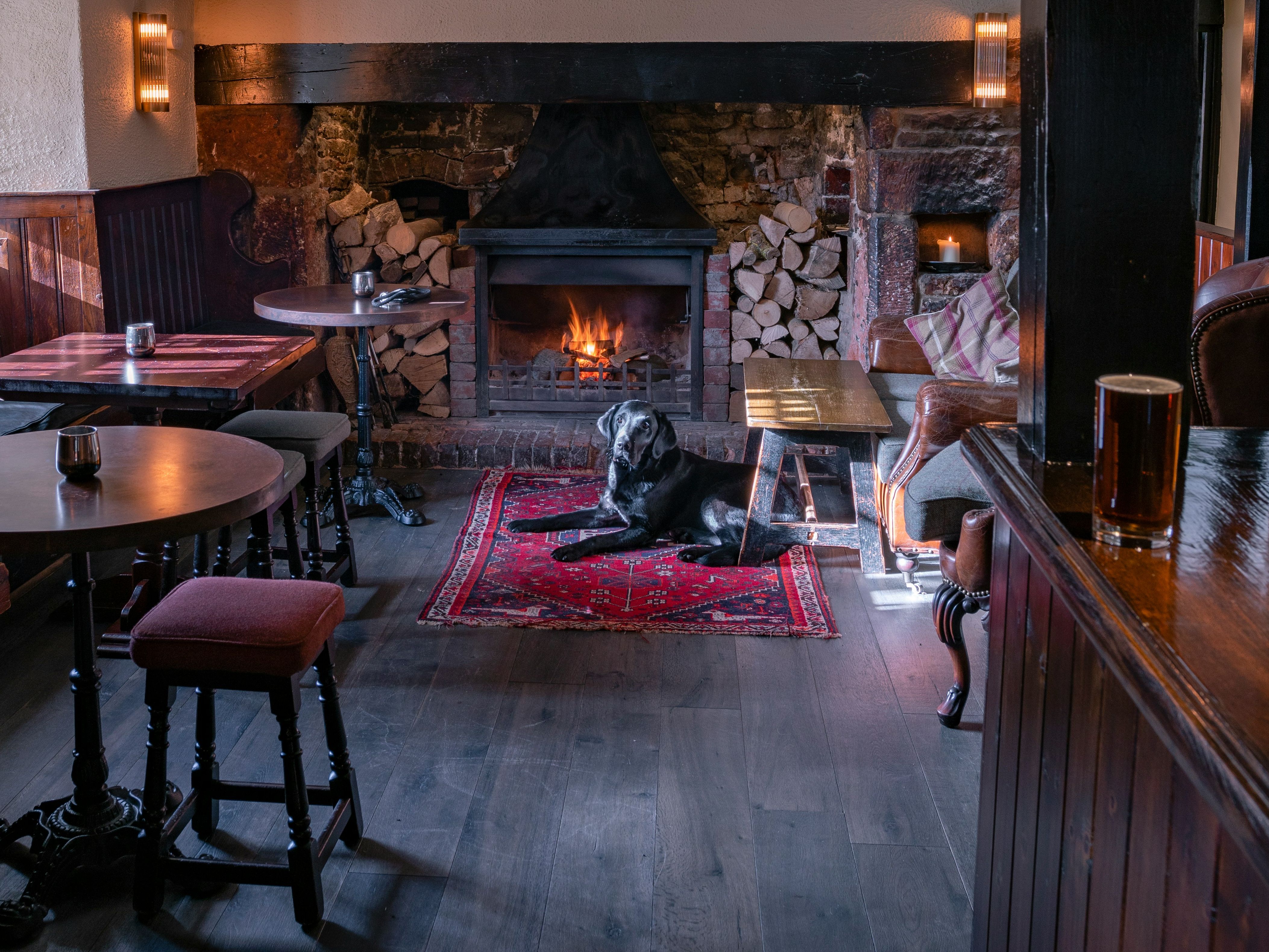 A cozy pub interior with a black dog lying on a red rug in front of a fireplace.
