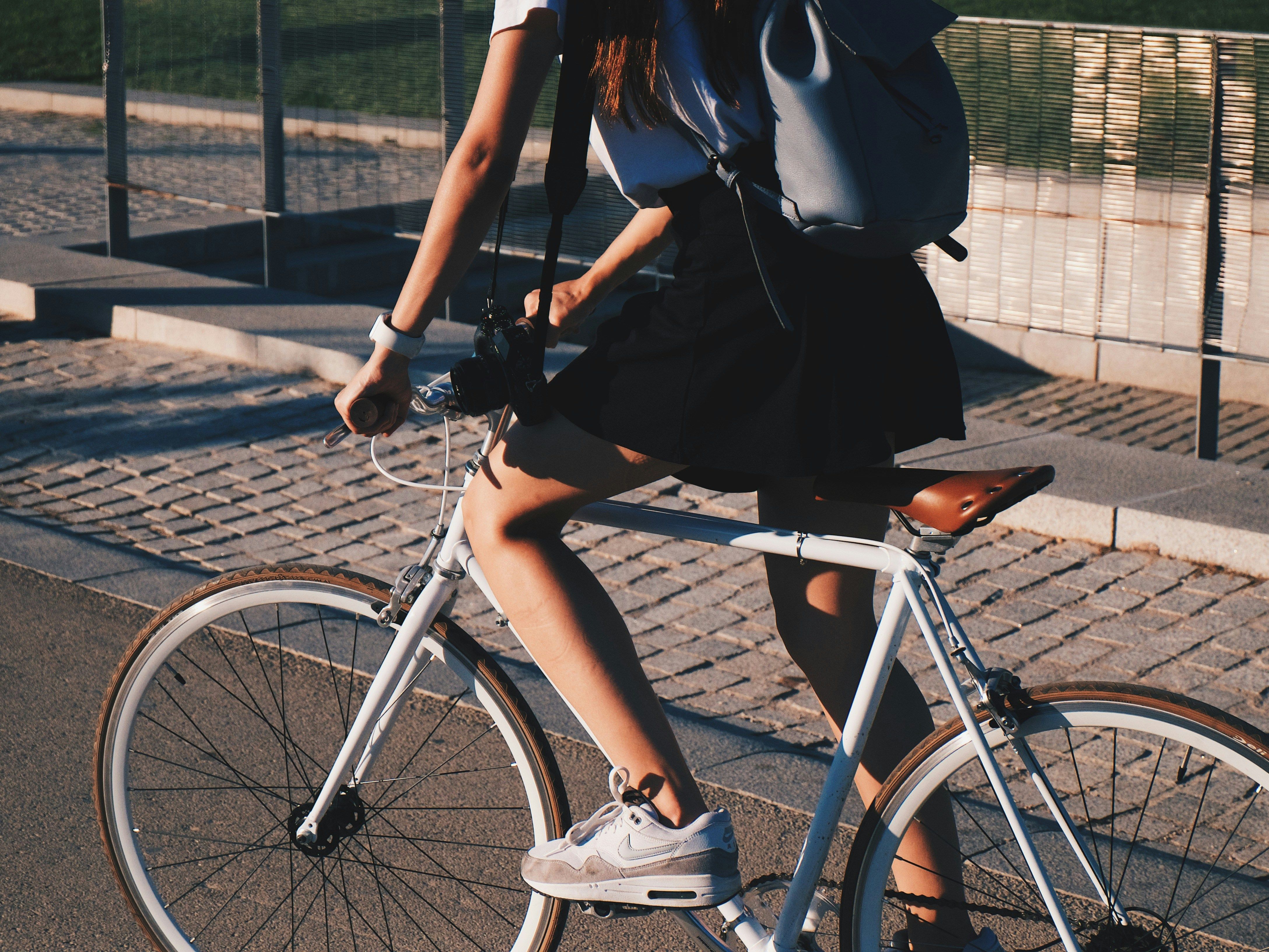 Person riding a white bicycle on a paved street with a backpack and camera.