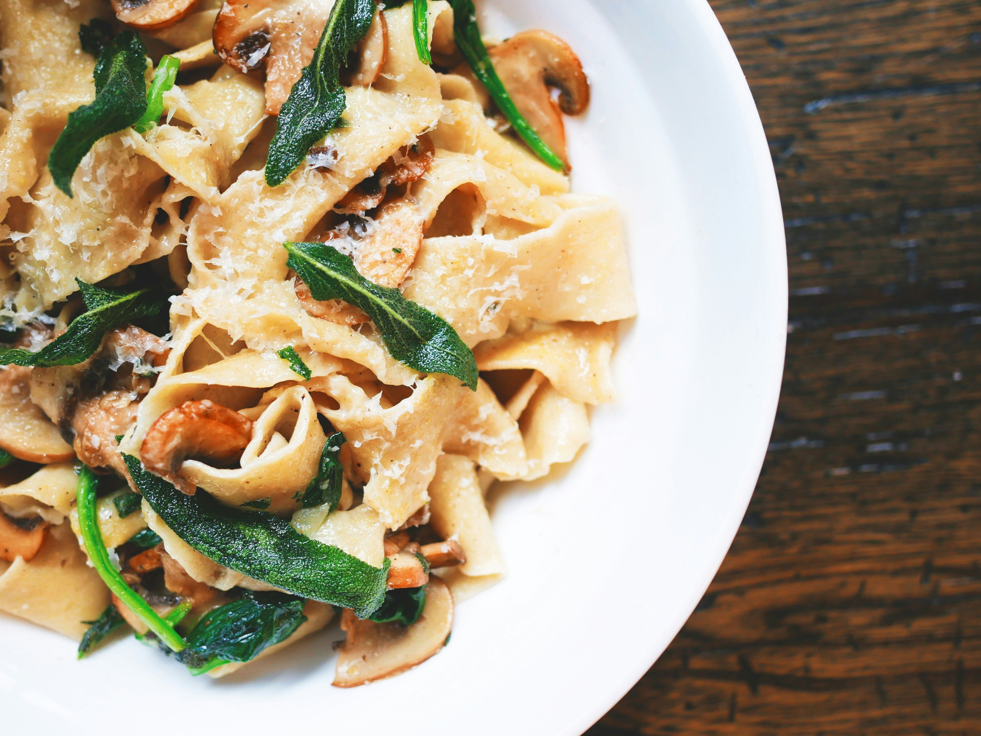 Close-up of a plate of pasta with mushrooms, greens, and grated cheese