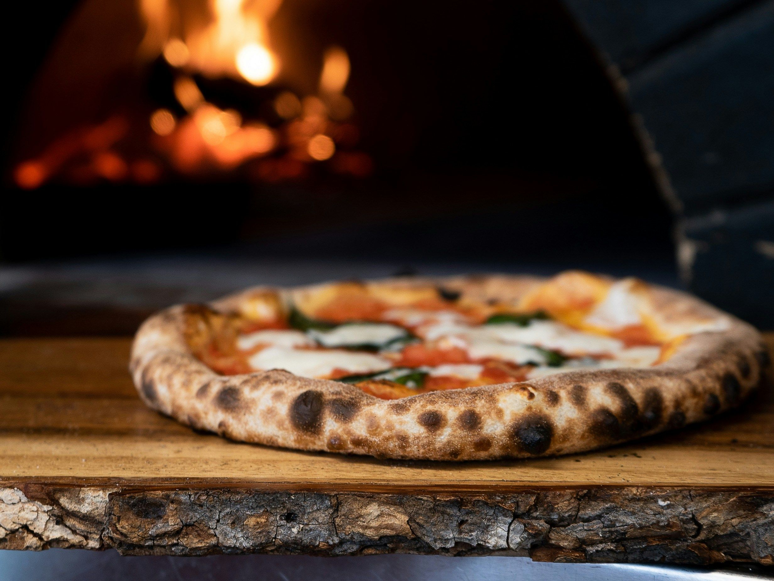 Traditional wood-fired pizza on a wooden board with a brick oven in the background