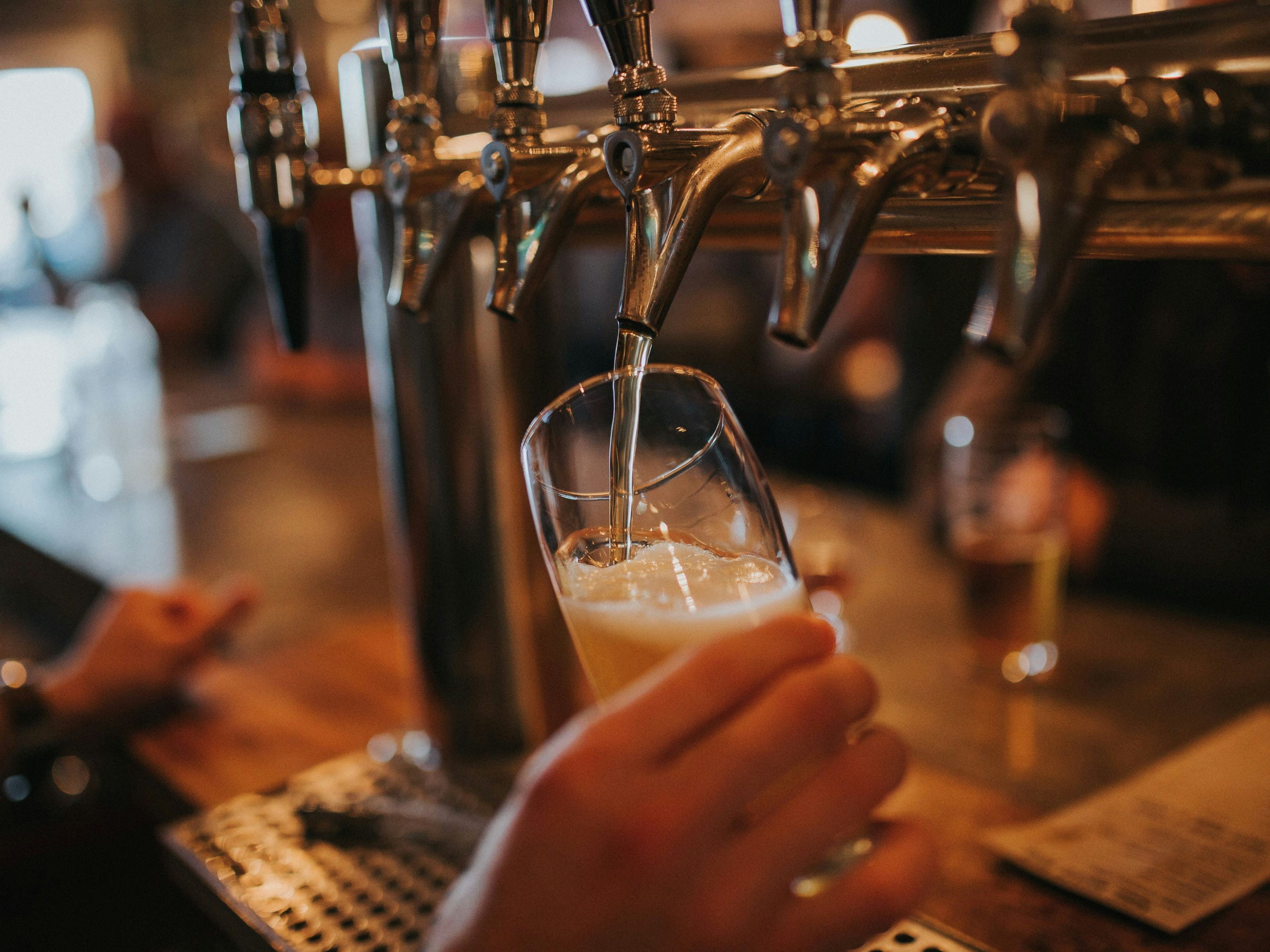 Close-up of a hand pouring beer from a tap into a glass at a bar.